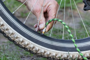 Yazın sokakta bisiklet tekerleği pompalayan bir adamın yakın çekimi. Adam pompa kullanarak bisiklet tekerleğini şişiriyor..