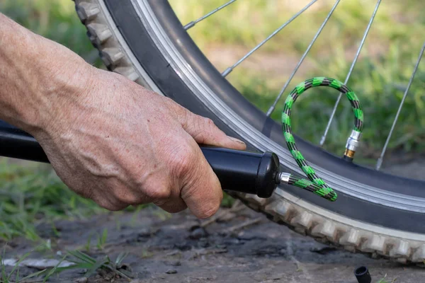 stock image Close-up of a man pumping bicycle wheel in nature. Man inflates bicycle wheel using a pump.