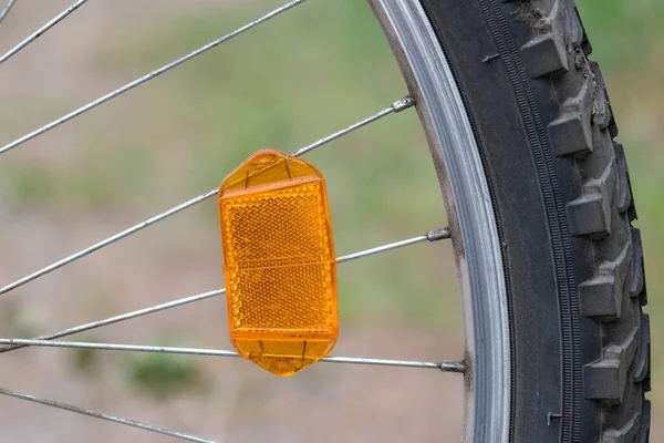 야외에 그라운드 장치와 겨루는 자전거 바퀴의 오렌지 플라스틱 반사기 — 스톡 사진