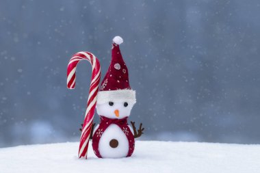Karlı arka planda oyuncak bir kardan adam olan bir Noel kompozisyonu. Yeni yıl kartları için tatil kavramı.