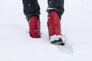 Kırmızı ayakkabılı bir kız kış mevsiminde karla kaplı bir parkta yürür..
