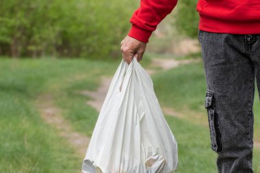 Bir adam elinde beyaz bir plastik torba tutuyor. Çevresel çöp kirliliği sorunu..