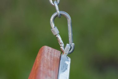 Sağlam bir metal karabina, büyük zinciri ahşap kirişe takar. Şehir parkında bir salıncakta sallanıyor..