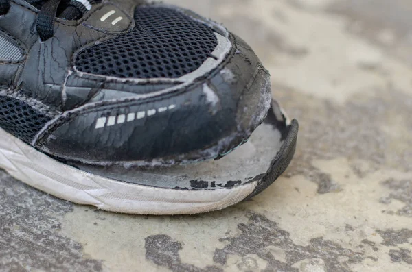 在地板上的特写镜头坏了的黑色旧运动鞋 — 图库照片