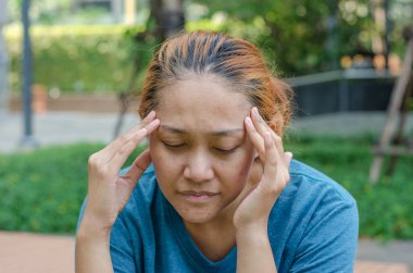 Parkta oturan Asyalı kadınlar şakaklarına dokunuyor, baş ağrısı ya da baş dönmesi hissediyorlar, yorgun hissediyorlar. Ağrı kesici lazım.