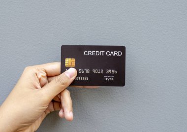 Gri bir arka plana yerleştirilmiş güvenlik çipi olan siyah bir kredi kartı modeli tutan bir kadın el.