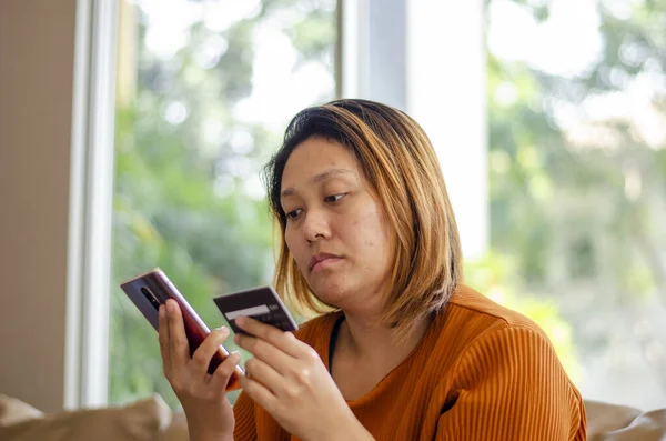 Asian woman falling victim to financial transaction, hand holding on credit card and mobile phone