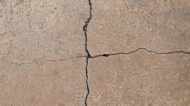 Çatlamış bir yüzeyin yakından görüntüsü, betondan yapılmış olabilir. Yüzeyin üzerinde belirgin bir çatlak olan pürüzlü bir dokusu var.