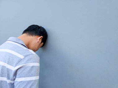 Asyalı bir adam umutsuzluk, stres ve üzüntü içinde kafasını duvara vuruyor..