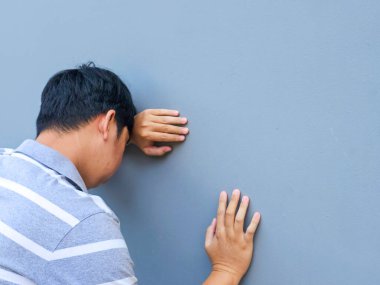 Asyalı adam ellerini umutsuzluk, stres ve üzüntü içinde duvara yaslar..