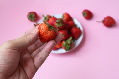 Arka planda bir tabak çilek olan bir çileği tutan el bulanık..