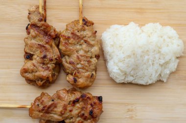 Yüksek açılı ızgara domuz şişi ve tahta tepside yapışkan pirinç manzarası. Tayland sokak yemeği.