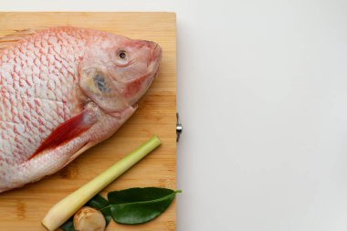 Kırmızı Tilapia balık kafası ve Galangal, limon otu, kaffir kireç yaprakları beyaz arka planda tahta bir tahtada. kopyalama alanı ile