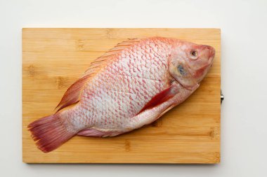 Beyaz arka planda tahta bir tahtada taze bir Red Tilapia balığı.