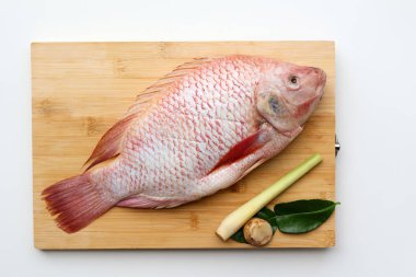 Taze bir Red Tilapia balığı ve Galangal, limon otu, kaffir kireç yaprakları beyaz arka planda tahta bir tahtada.