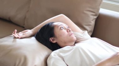 Asyalı kadın üzgün, depresif ve mutsuz bir yüzle kanepede yatıyor. Depresyona girmiş olabilir.