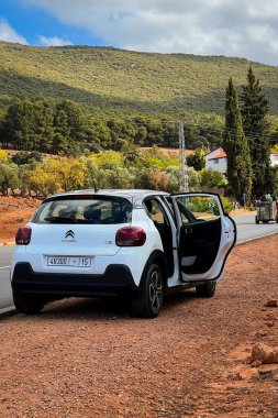 Citroen C3 arabası yol kenarına park edilmiş ve kırsal alanda açık bir kapısı var.