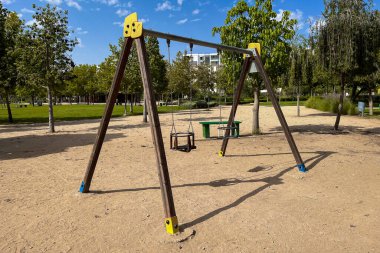 Arka planda ağaçlar olan parkta boş bir salıncak.