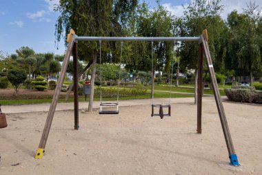 Arka planda ağaçlar olan parkta boş bir salıncak.
