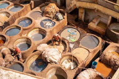 Man working as a tanner in the dye pots at leather tannery in the old medina of Fez clipart