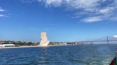 Keşifler Anıtı ve 25 Nisan 'da Lizbon' daki Köprü üzerinde hareket eden bir feribot görüntüsü