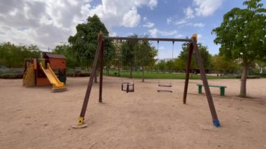 Arka planda ağaçlar olan parkta boş bir salıncak.