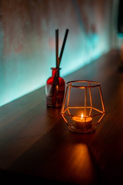 Ahşap bir masada, metal bir tutacağın içindeki samimi bir mumun yakın çekimi.