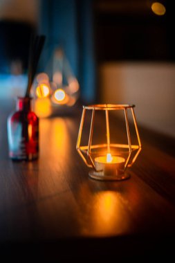 Ahşap bir masada, metal bir tutacağın içindeki samimi bir mumun yakın çekimi.