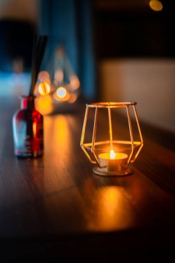 Ahşap bir masada, metal bir tutacağın içindeki samimi bir mumun yakın çekimi.