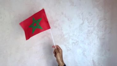 Fas bayrağını tutan ve arka planda bir duvarla sallayan bir el.