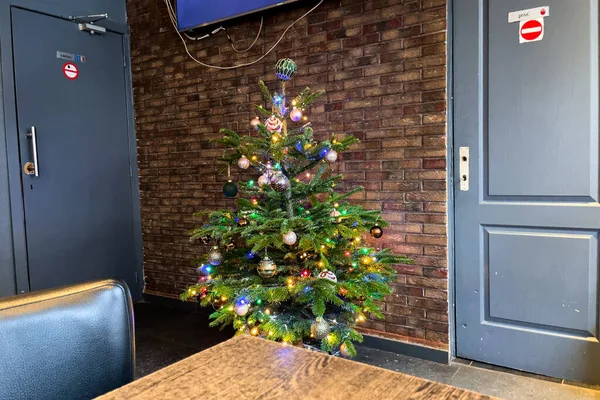 Small Christmas tree decorated with colorful balls and lights inside a restaurant