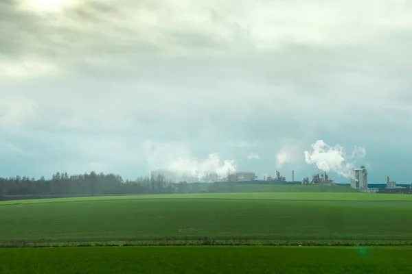 Factory exhausting co2 emissions into the air with a green field in the foreground in Brussels, Belgium
