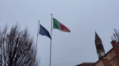 Italian flag and a European union flag waving with cloudy sky in the background