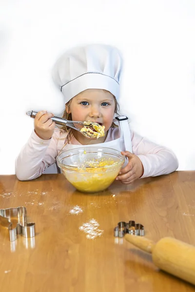 Little girl cook in an apron and a cap, holds a whisk with dough, a cup . The concept of food, restaurant, training, poster, postcard, health, diet, nutrition,copy space, layout, hobby,job,advertising