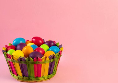 Easter layout . Multi-colored eggs lie in a wicker basket, pink background. Holiday concept, congratulation, postcard, template,copy space, text, moc-up,handmade,spring,decoration,party,poster.