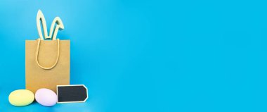 Paskalya bayrağı boş. Tavşanın kulaklarını dışarı çıkaran bir kese kağıdı, mavi arka planda yumurta ve bir tabak. Tatil kavramı, kartpostal, şablon, kopyalama alanı, metin, bahar, poster, satış, tasarım, model.