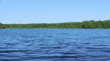 Manzara gölü, sudaki dalgalar, ağaçlar yeşil ve mavi gökyüzü. Doğa, çevre, turizm, dinlenme, rahatlama, meditasyon, temiz hava, yürüyüş, bakım, ekoloji, su kaynakları, su kaynakları kavramı