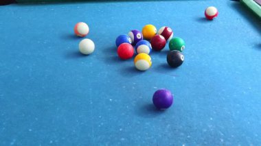 Üçgen şeklinde dizilmiş renkli toplarla dolu bir bilardo masasının yakın çekim görüntüsü. Toplar çarpmanın yan taraflarına sıçrıyor mavi keçeli yüzey topların canlı renkleriyle çelişiyor..