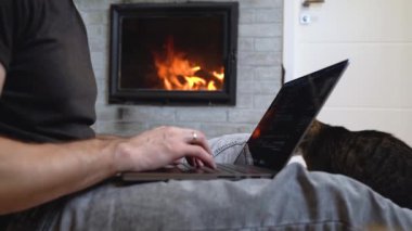 Home-working man types code by fire with cat companion
