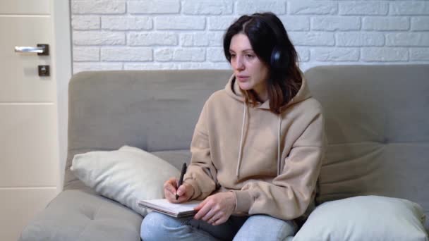 Γυναίκα Ακουστικά Σημειώνει Σημειώσεις Ένα Σημειωματάριο Ενώ Μελέτη — Αρχείο Βίντεο