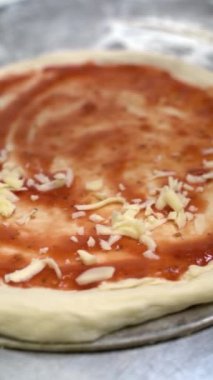 Yakın plan bir şef pizzanın üzerine rendelenmiş peynir serpiyor.