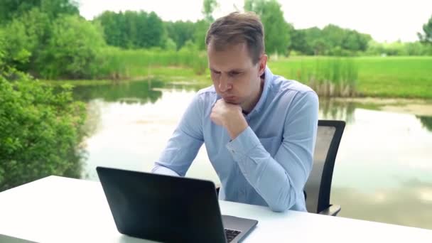男は川の近くの自然の中でオフィスデスクで働いています — ストック動画
