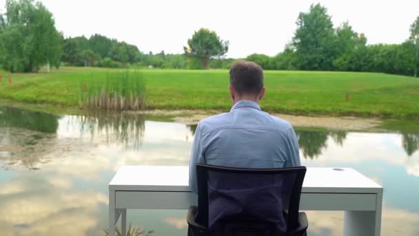 Ένας Άντρας Δουλεύει Ένα Γραφείο Στη Φύση Κοντά Ένα Ποτάμι — Αρχείο Βίντεο