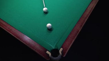 Yeşil kumaş üzerinde bilardo oyunu, bir adam bilardo topuna vuruyor.