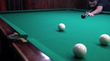 Bir adam bilardo topuna vurup diğerini vuruyor ve topu cebine atıyor.