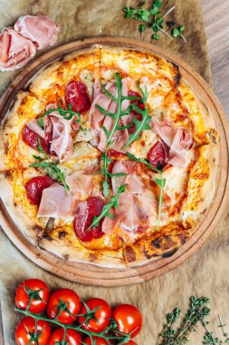 İştah açıcı bir pizza sunumu. İçinde pişirilmiş etler, yeşiller ve canlı domatesler var.