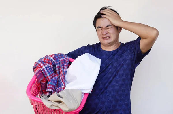 Asian man holds basket of cloth  for laundry, feels lazy, angry ,tired, put hand on head. Concept, daily chore, housework. Man doesn\'t want to wash clothes. Make funny face.