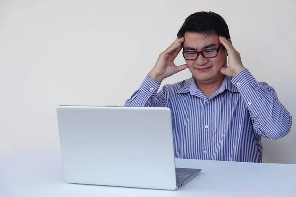 Asian middle-aged man office worker feels heachache, looks serious, think and plan something during working on laptop computer. Concept : Health problems , work with data.