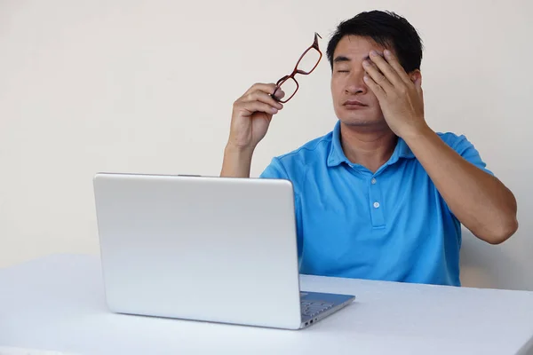 Asian man, feels hurt his eyes, holds eyeglasses during working on laptop. concept : Eyesight problem. Optometry. Glasses with convex or concave lenses. Myopia.Eye disease