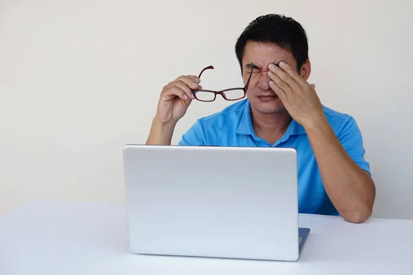 Asian man, feels hurt his eyes, holds eyeglasses during working on laptop. concept : Eyesight problem. Optometry. Glasses with convex or concave lenses. Myopia.Eye disease